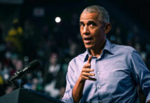 Obama DARES Dems To Do THIS?! Barack Obama in blue shirt speaking at podium with microphone.