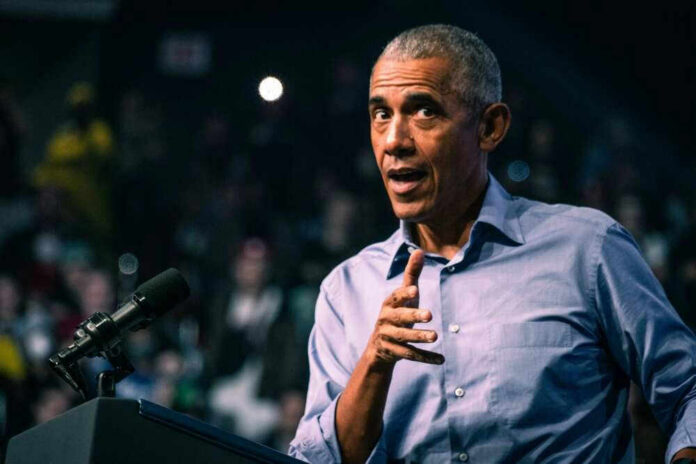 shutterstock_2231134745 Barack Obama in blue shirt speaking at podium with microphone.