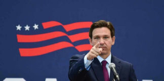 Governor of Florida, Ron DeSantis points forward at podium.