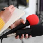 Label Oops Triggers Meatloaf Meltdown Journalist holding two microphones while writing in a notebook