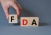 FDA Slams THESE Cheap Weight Loss Drugs? A hand holding a wooden block with the letter F, next to blocks spelling FDA