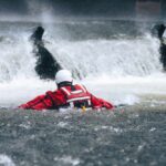 Harbor Fight Turns Deadly Rescuer in red gear navigating turbulent water near a waterfall