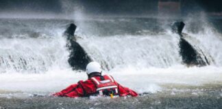 Rescuer in red gear navigating turbulent water near a waterfall
