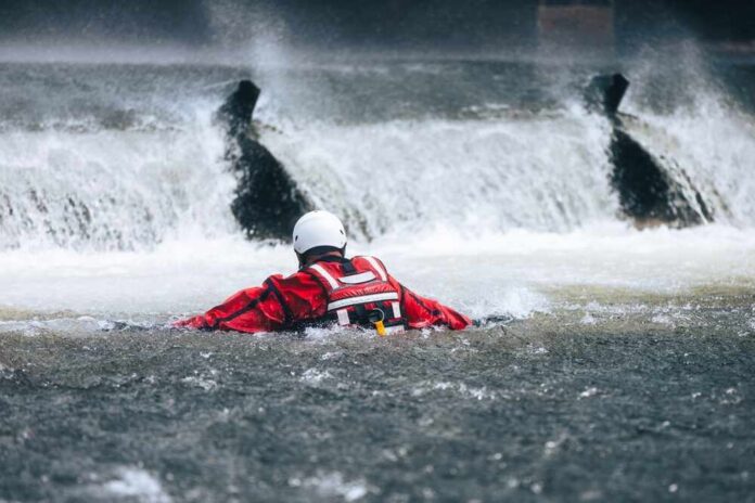 Rescuer in red gear navigating turbulent water near a waterfall
