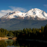Tourist Vanishes — Body Found In Mountains Snow-capped mountain above a forested lake with a small arched bridge
