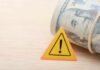 Taxpayer Rage: $9.5B For No Work A roll of cash next to a warning sign on a wooden surface