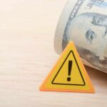Taxpayer Rage: $9.5B For No Work A roll of cash next to a warning sign on a wooden surface