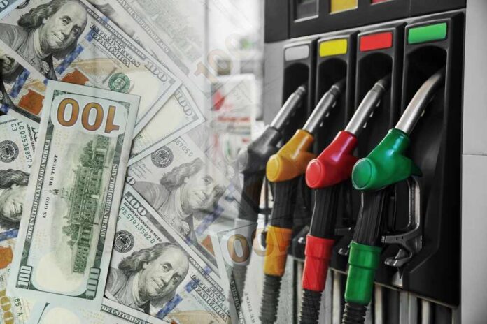 Fuel pump nozzles next to spread of U.S. hundred-dollar bills