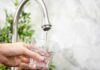 Abortion Pills in Tap Water? Hand holding a glass under a kitchen faucet as water pours in
