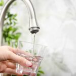 Abortion Pills in Tap Water? Hand holding a glass under a kitchen faucet as water pours in