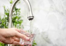 Hand holding a glass under a kitchen faucet as water pours in