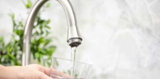 Hand holding a glass under a kitchen faucet as water pours in