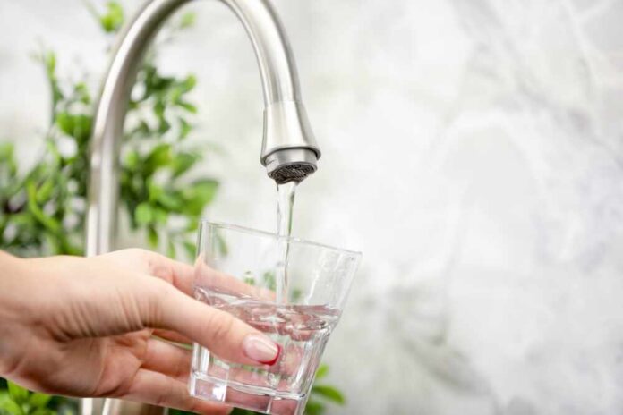 Water,Saving,Concept.,Woman,Filling,Glass,With,Tap,Water,Indoors, Hand holding a glass under a kitchen faucet as water pours in