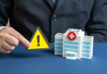 Hospital Drug Tied To Adult Death Spike A business professional holding a warning sign next to a model of a hospital