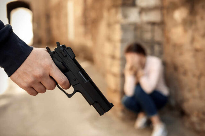 Armed,Man,Holding,Woman,Hostage,Outdoors,,Focus,On,Hand,With Hand holding a handgun with a distressed person in the background