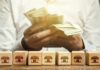 Person counting cash with wooden blocks depicting store icons