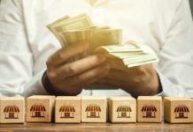 Bill Shock Spreads – Is Water Next? Person counting cash with wooden blocks depicting store icons