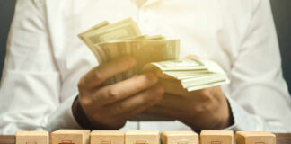 Person counting cash with wooden blocks depicting store icons
