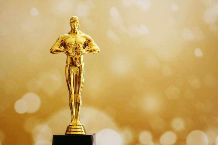 shutterstock_2119939280 Golden Oscar trophy against a sparkling gold background.