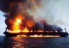 Large ship engulfed in flames on the ocean.