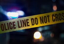 Campus Death Probe Snags Vape Duo Police tape with blurred emergency lights in the background