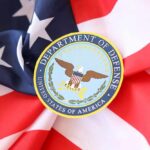 DOD’s Livestream Promise Sparks Fury Soldiers in uniform facing American flag outdoors.