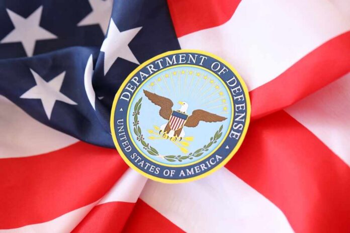 Soldiers in uniform facing American flag outdoors.