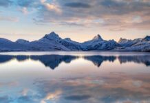 Alps Meltdown: Two Years, Vanished Ice Snow-capped mountains reflected in a calm lake at sunrise