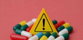 Warning sign among assorted capsules on pink background